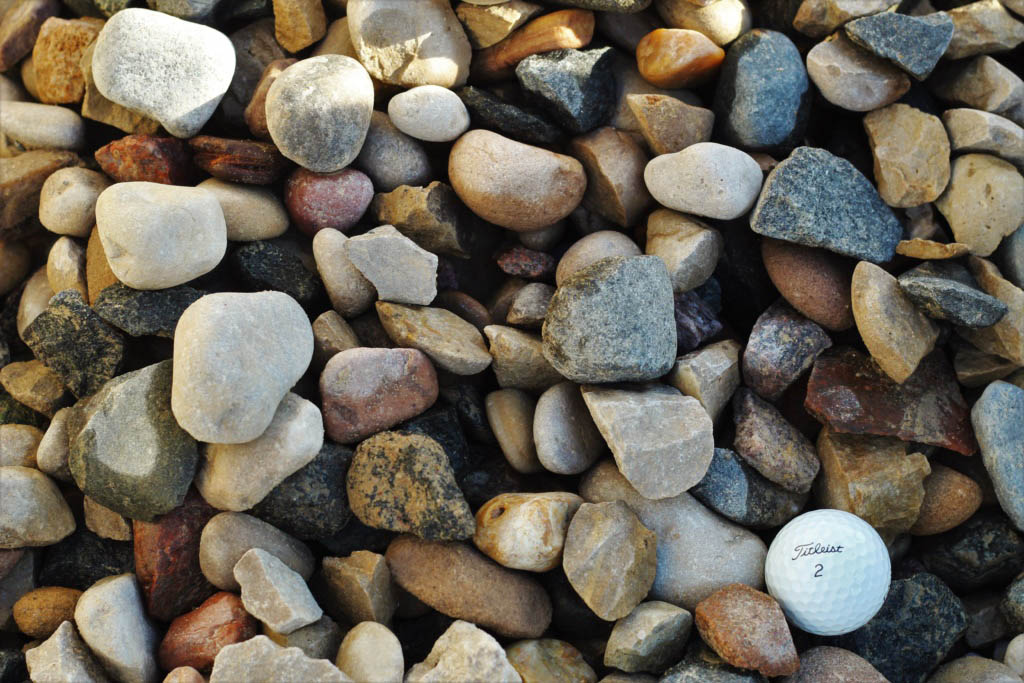 A variety of multicolored rocks and pebbles of different shapes and sizes with a white Titleist golf ball for scale.