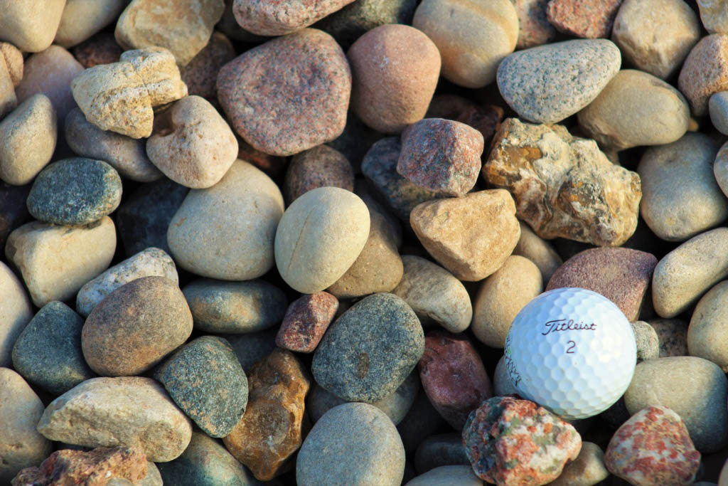 Close-up of an assortment of smooth, natural-colored stones with a white Titleist golf ball number 2, resting among them to provide scale.