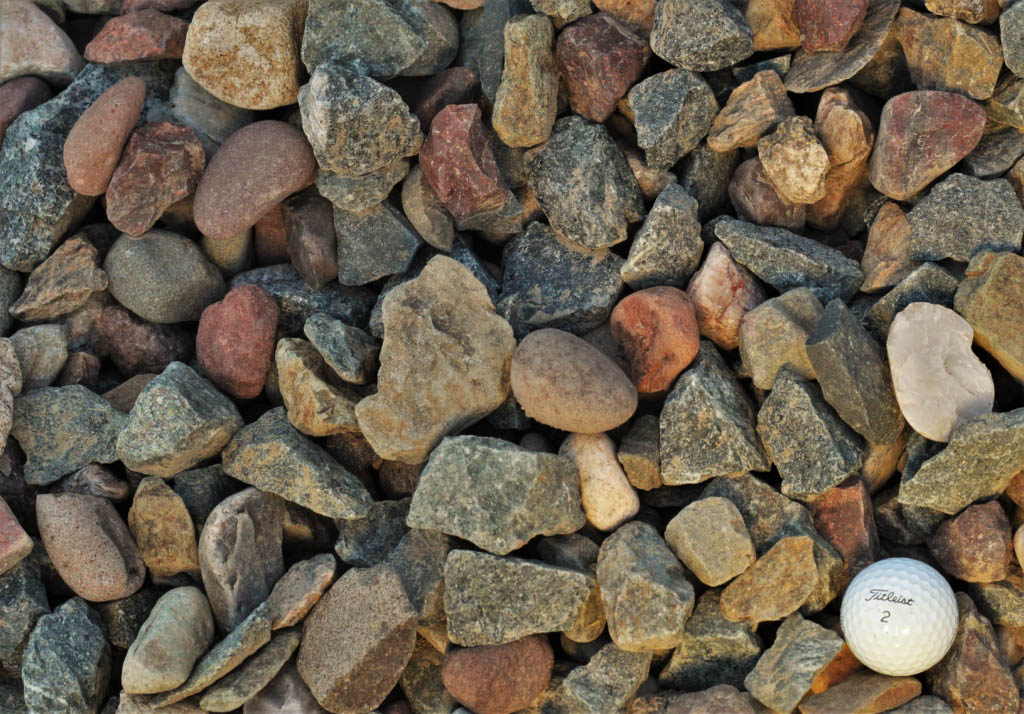 A variety of jagged and rounded rocks in earth tones with a white Titleist number 2 golf ball nestled among them for scale.
